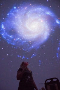 Chelsea Sharon pointing at an image of a galaxy in a darkened planetarium.
